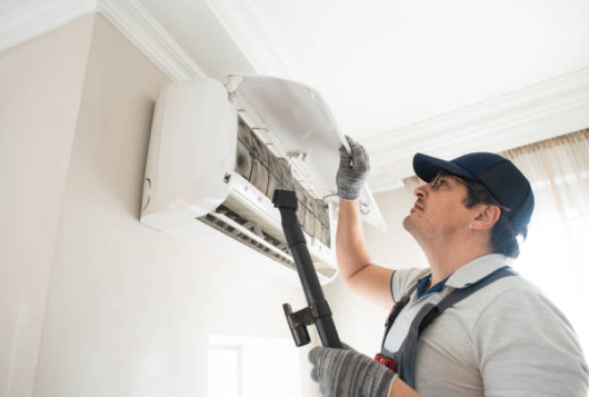 HVAC technician cleaning a wall mounted mini split air conditioner during maintenance by Green Energy Mechanical in Canton MA.