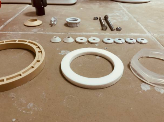 A collection of plumbing repair parts, including rubber gaskets, plastic washers, and metal bolts, is laid out neatly on a tiled surface.