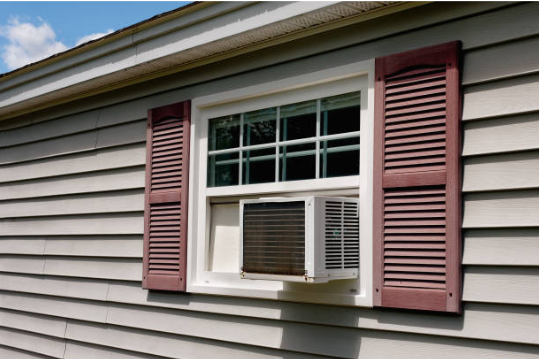 A window-mounted air conditioner installed in a residential home with exterior siding and decorative shutters.