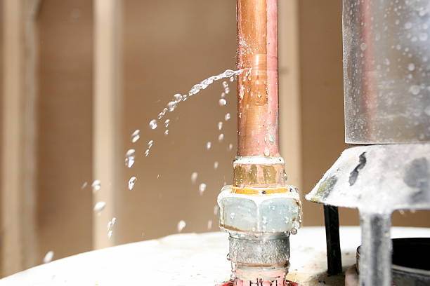 Copper pipe spraying water from a leaking fitting on top of a water heater