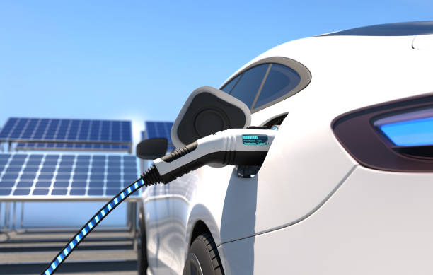 White electric car plugged into a charger with solar panels in the background