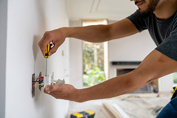 Electrician using a yellow-handled screwdriver to install a wall outlet during a home renovation