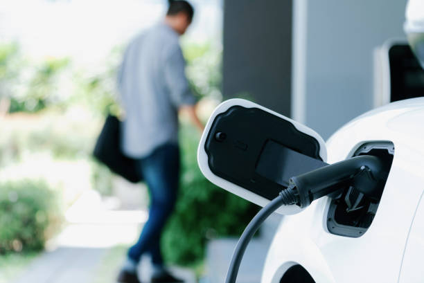 Charging plug connected to a white electric car while a man walks away in the background