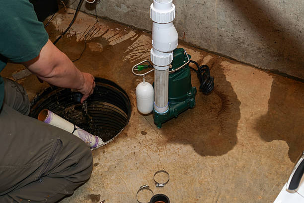 A technician servicing a basement sump pump system by inspecting the sump pit and pump components to help prevent water damage and flooding.