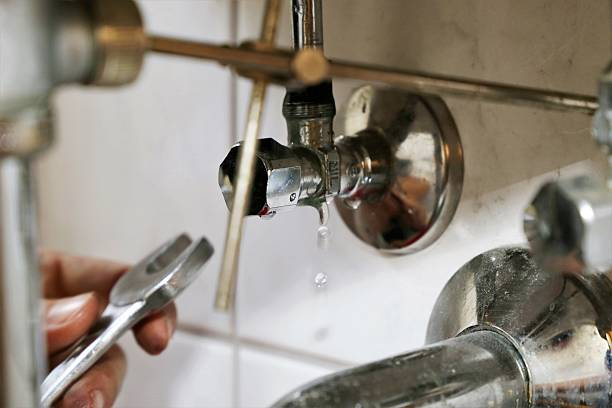 Plumber's hand holding a wrench near a dripping chrome shutoff valve