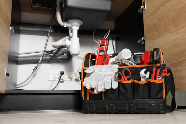 Tool bag filled with plumbing supplies and gloves placed on the floor beneath an under-sink pipe installation