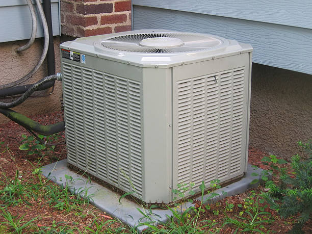 Beige residential AC condenser unit on a pad beside a house with mulch and grass